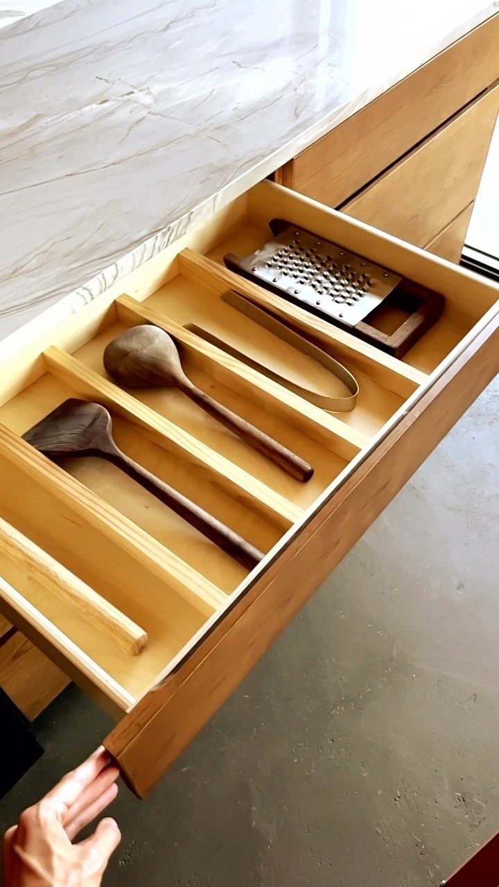 Open wooden kitchen drawer containing wooden spoons and metal cooking utensils.