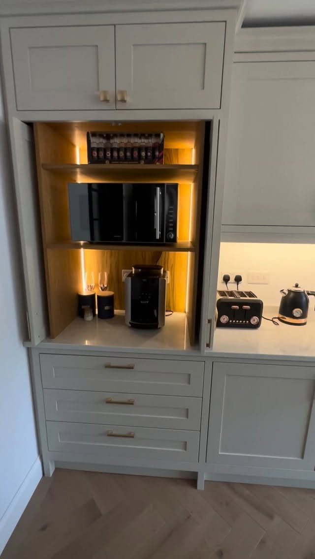 Light grey kitchen cabinet with integrated lighting housing a coffee machine and microwave.