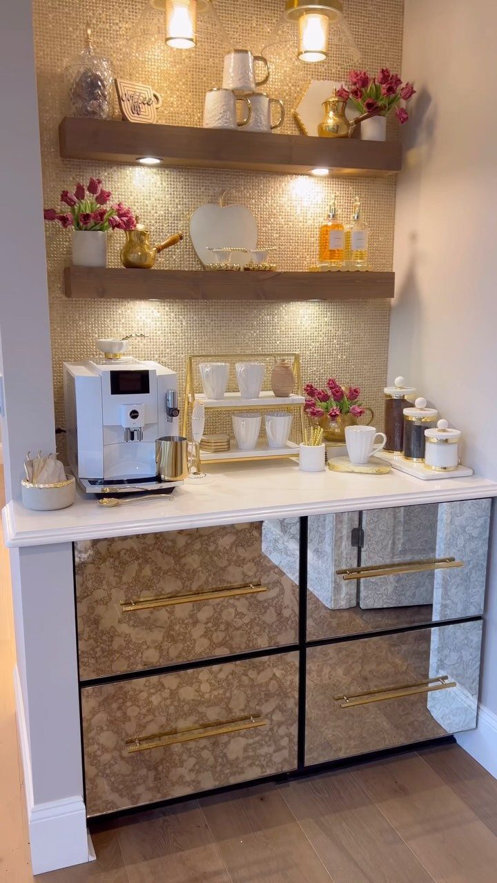 Modern coffee station with white espresso machine, gold shelves, and pink potted flowers.