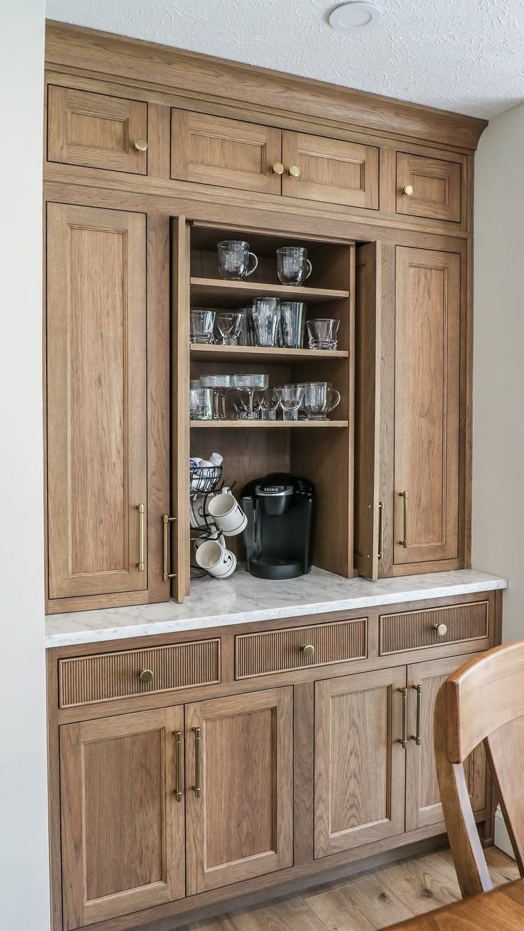 Built-in light wood coffee station with sliding pocket doors and marble countertop