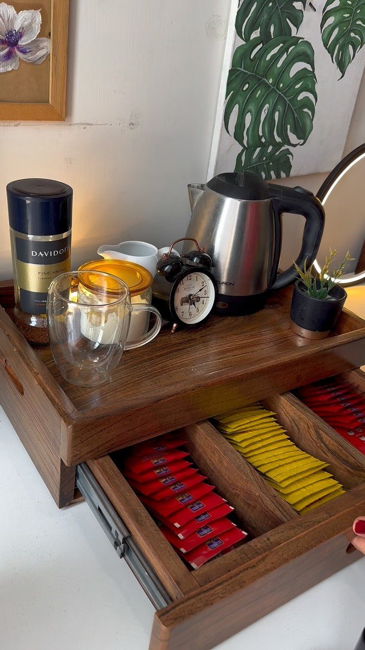 Wooden coffee station tray with electric kettle, tea packets, and a glass mug.