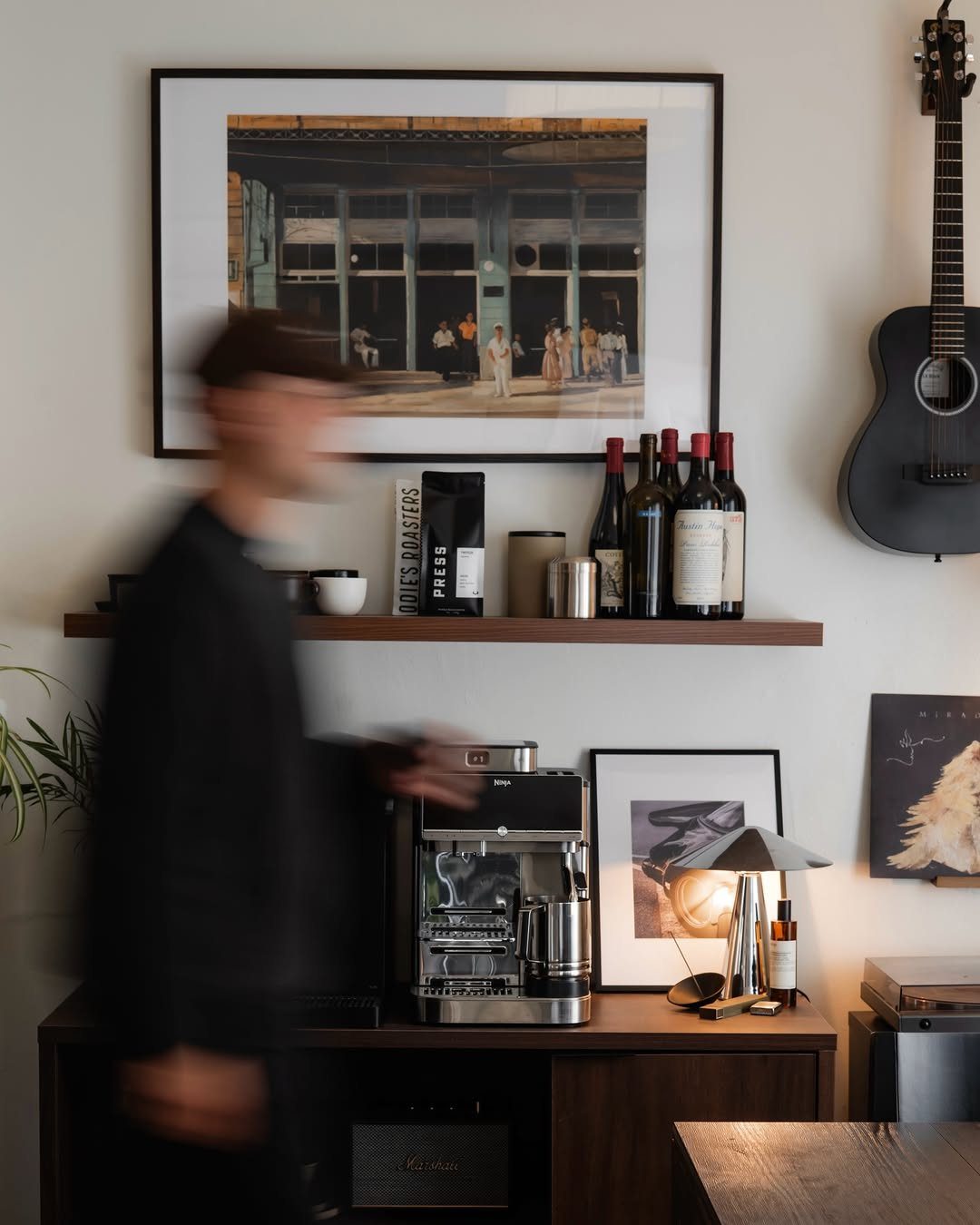 Silver espresso machine on a dark wood sideboard with a floating shelf above.