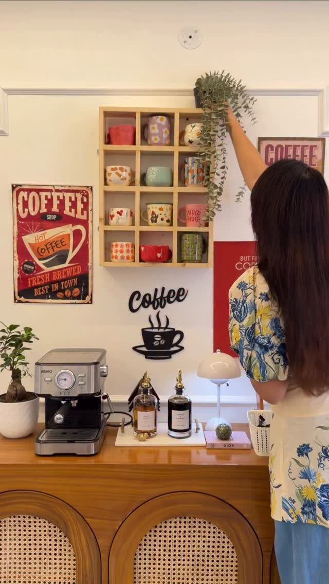 Woman arranging a plant above a coffee station with open mug shelves.