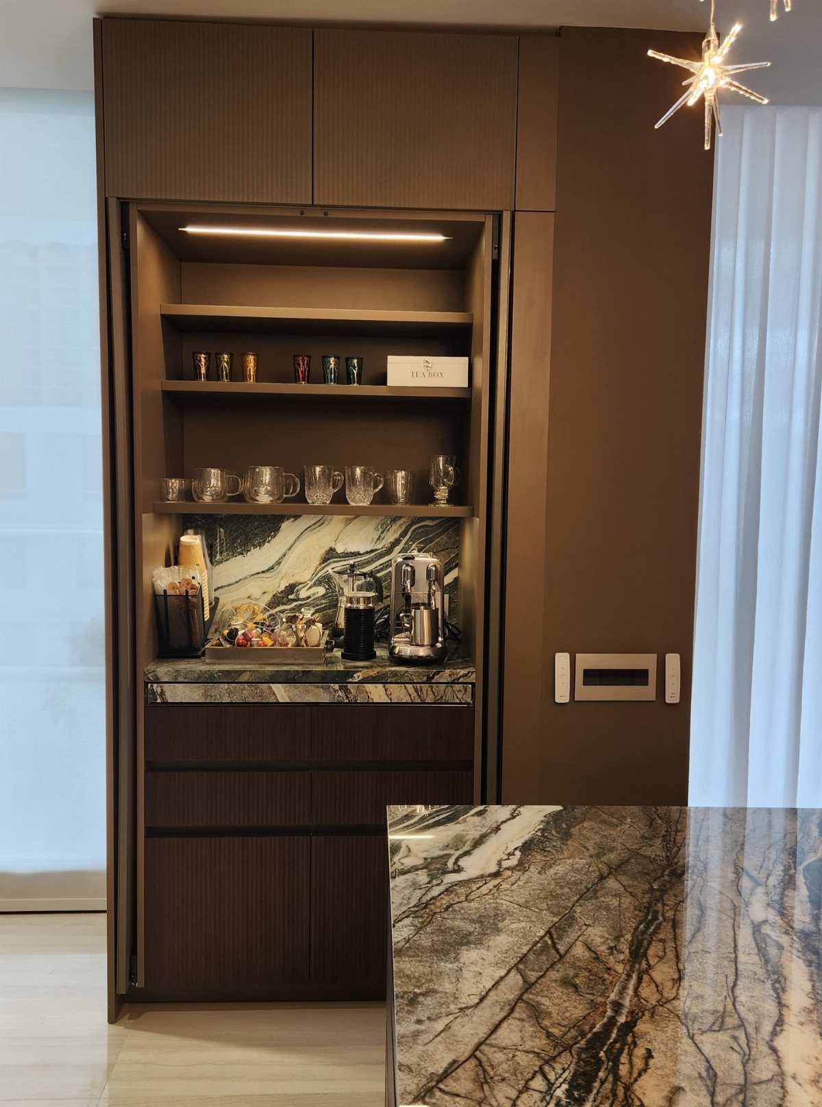 Built-in coffee station with dark brown cabinetry, marble backsplash, and espresso machine.