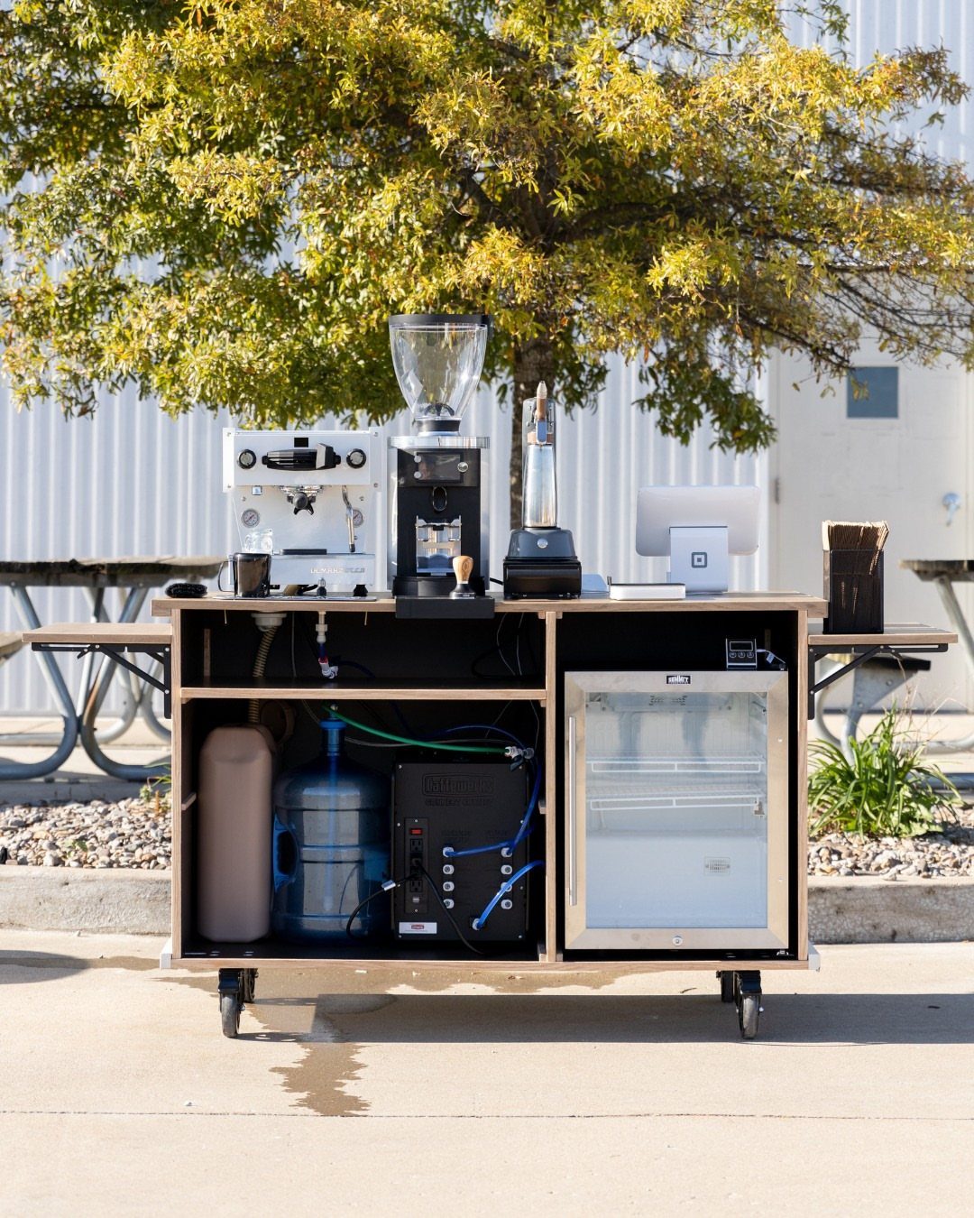 Mobile coffee station on wheels with espresso machine and small refrigerator outdoors