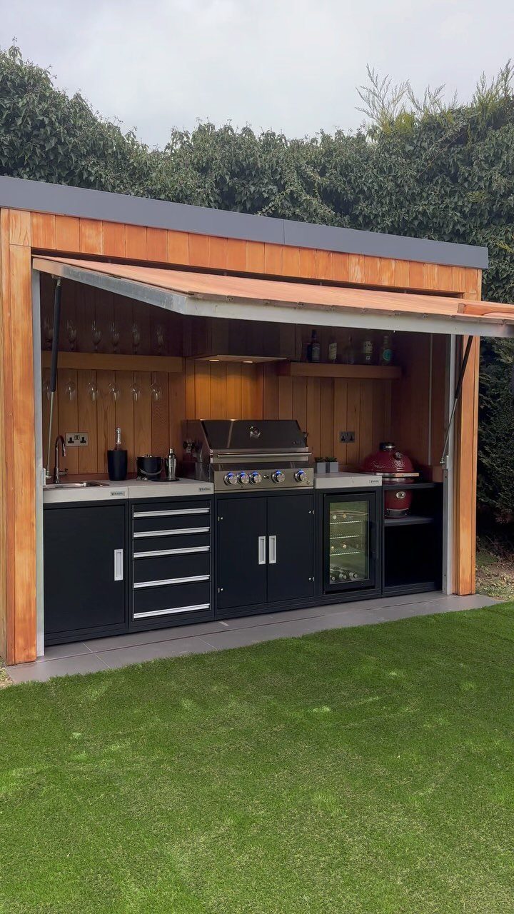 Outdoor kitchen with black cabinets and wooden backsplash under a wooden awning.