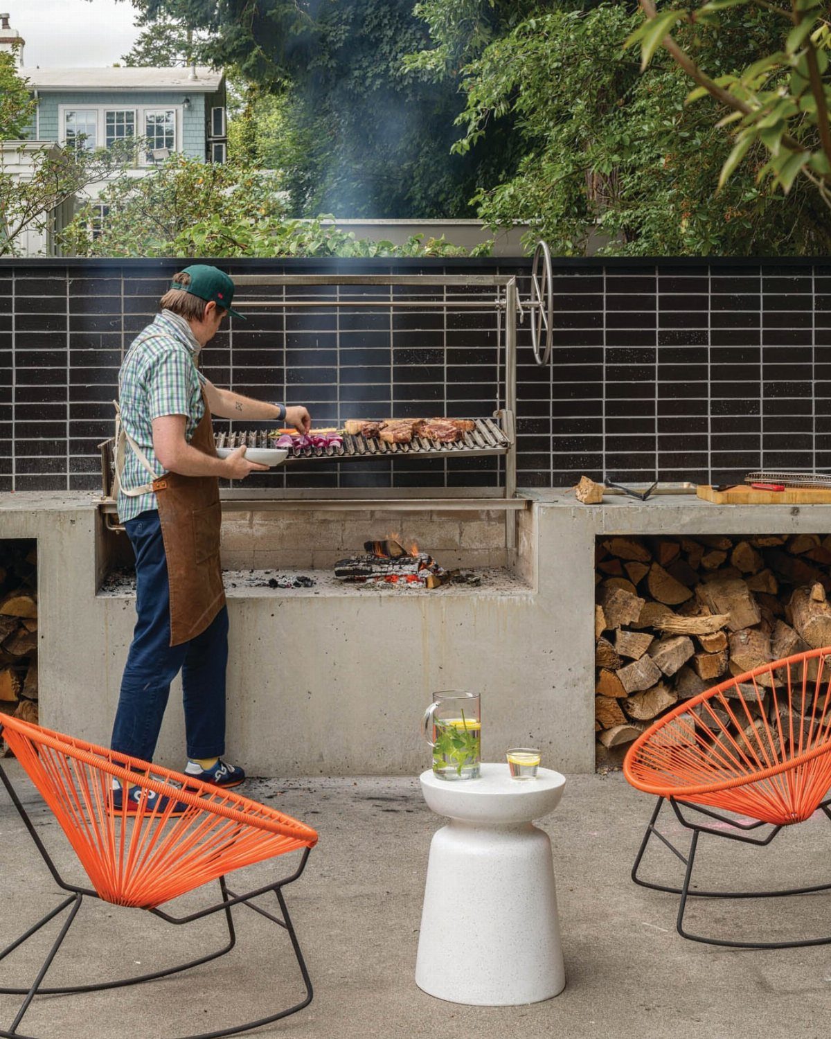 Man grilling meat in front of a dark tiled outdoor kitchen backsplash wall
