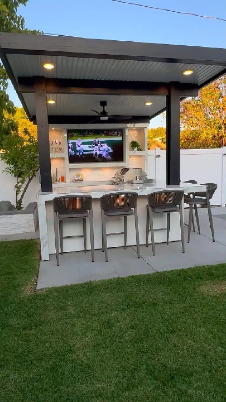 Covered outdoor bar with marble countertop, grey stools, and mounted television on patio.