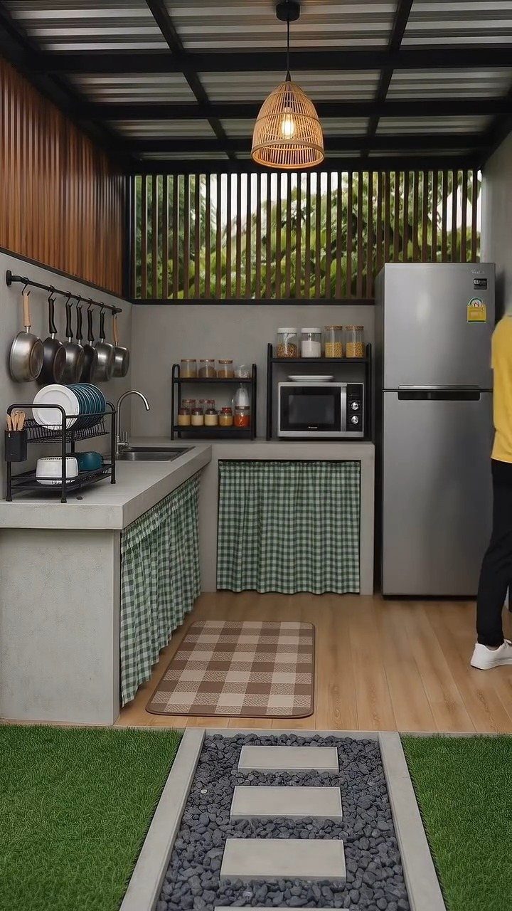 Compact outdoor kitchen with concrete counters, stainless steel fridge, and woven pendant light.