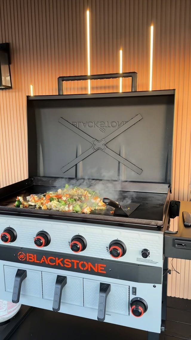 Blackstone outdoor griddle cooking mixed vegetables against a wood-paneled wall with lighting