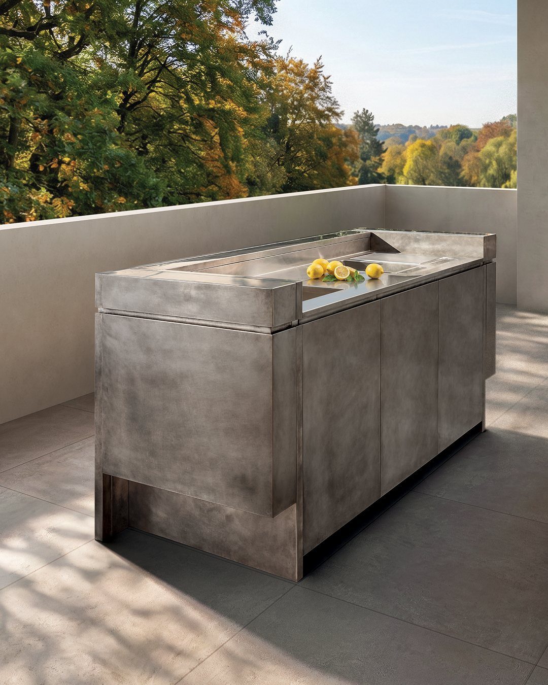 Metallic outdoor kitchen island with built-in sink on a patio overlooking autumn trees