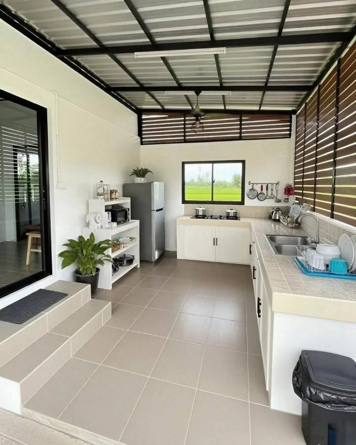Minimalist outdoor kitchen with white cabinetry, beige counters, and a corrugated metal roof.
