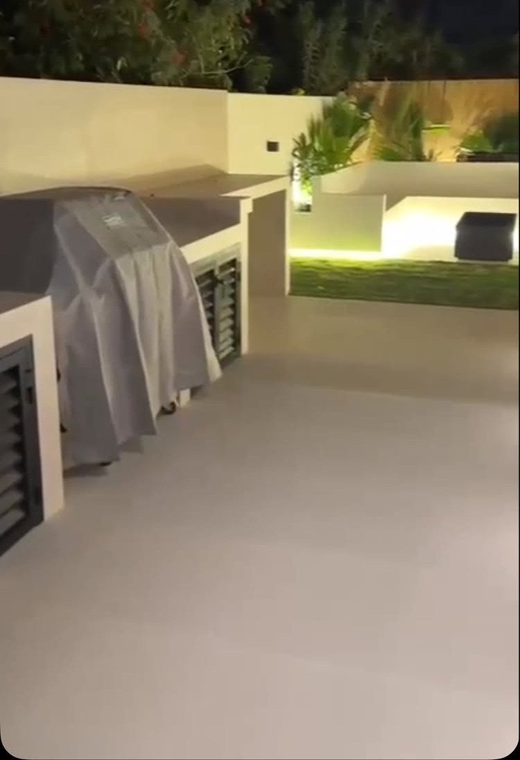 Modern outdoor kitchen at night featuring warm LED under-bench lighting and covered grill.