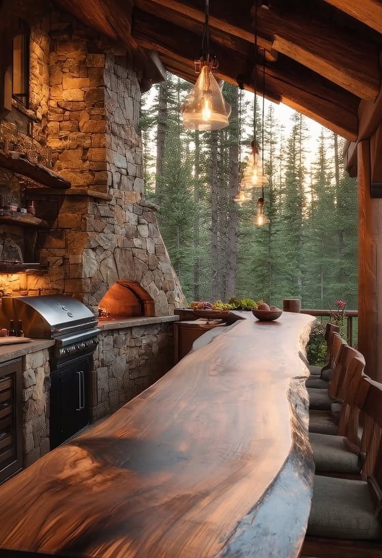 Rustic outdoor kitchen with stone walls, live-edge wood bar, and forest view.