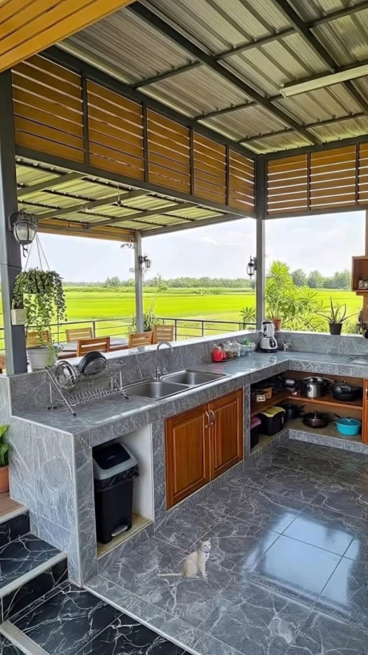 Outdoor kitchen with marble counters and wooden cabinets overlooking a green tropical field
