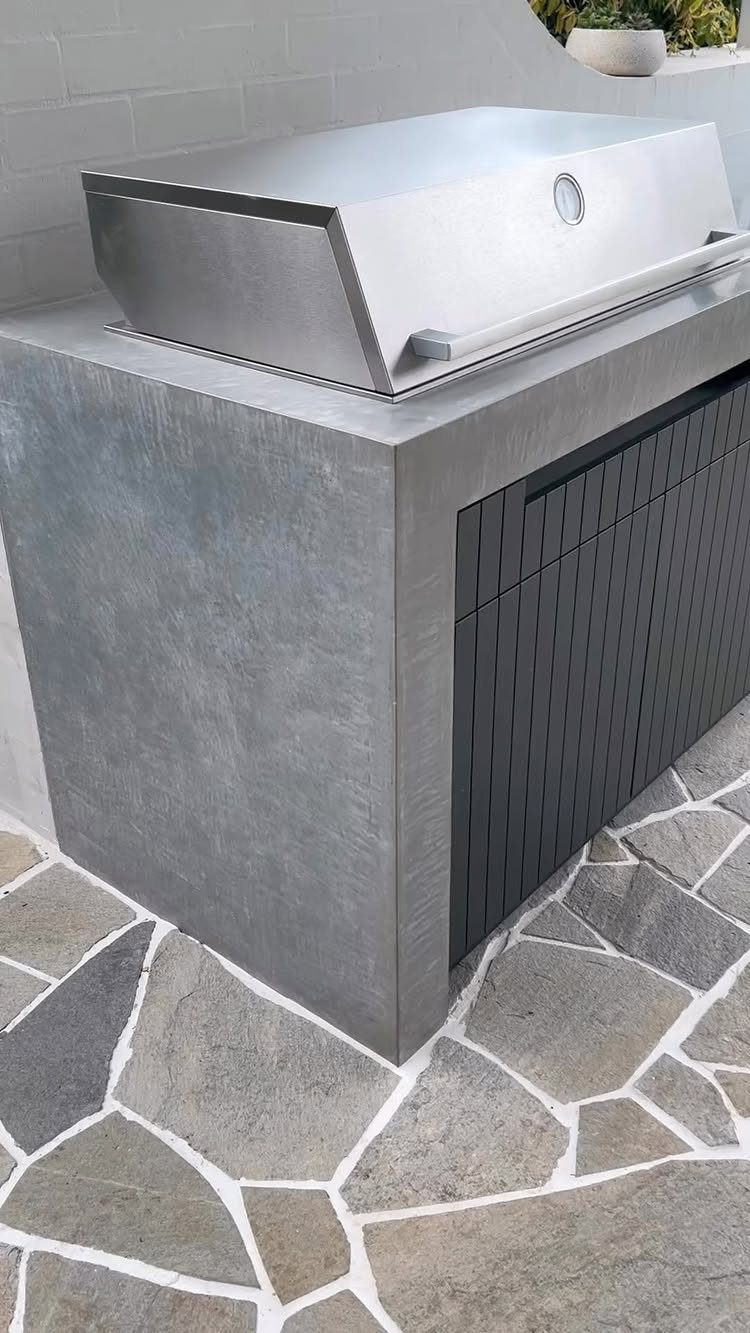 Modern outdoor kitchen with stainless steel grill and grey concrete base on flagstone patio