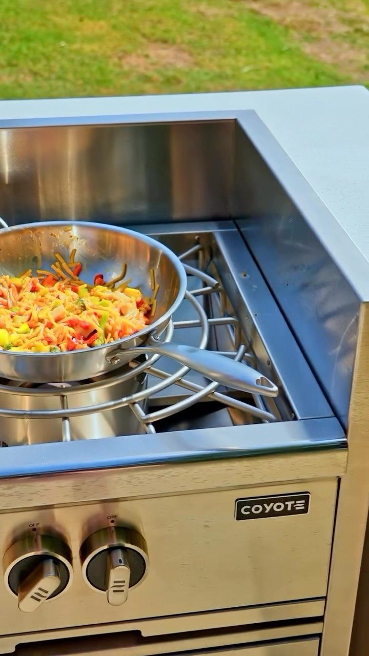 Stainless steel outdoor gas burner with a pan of colorful sautéed vegetables.