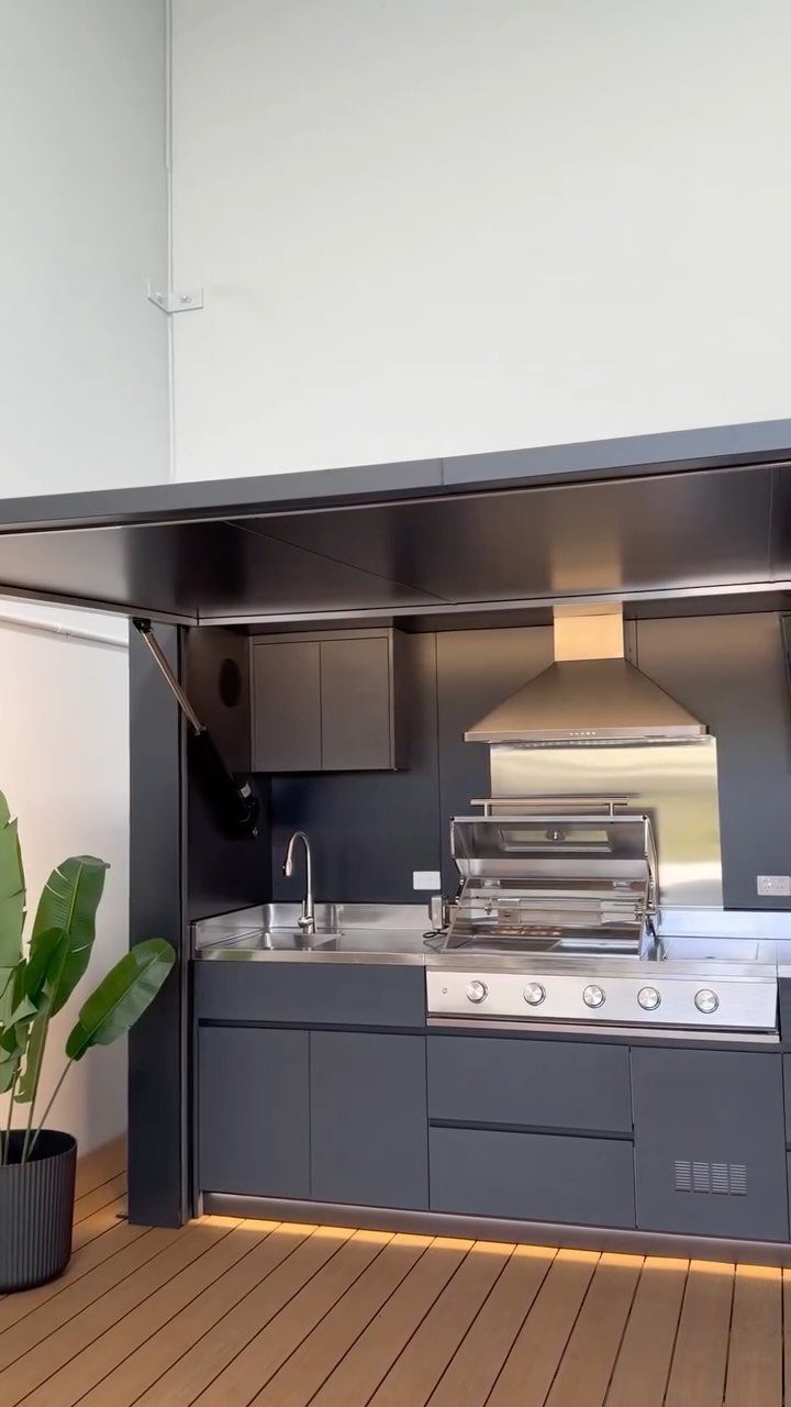 Modern outdoor kitchen with integrated stainless steel grill and dark grey cabinetry.