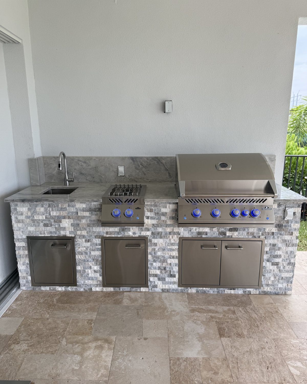 Outdoor kitchen with natural stone countertops, built-in grill, and stacked stone base.