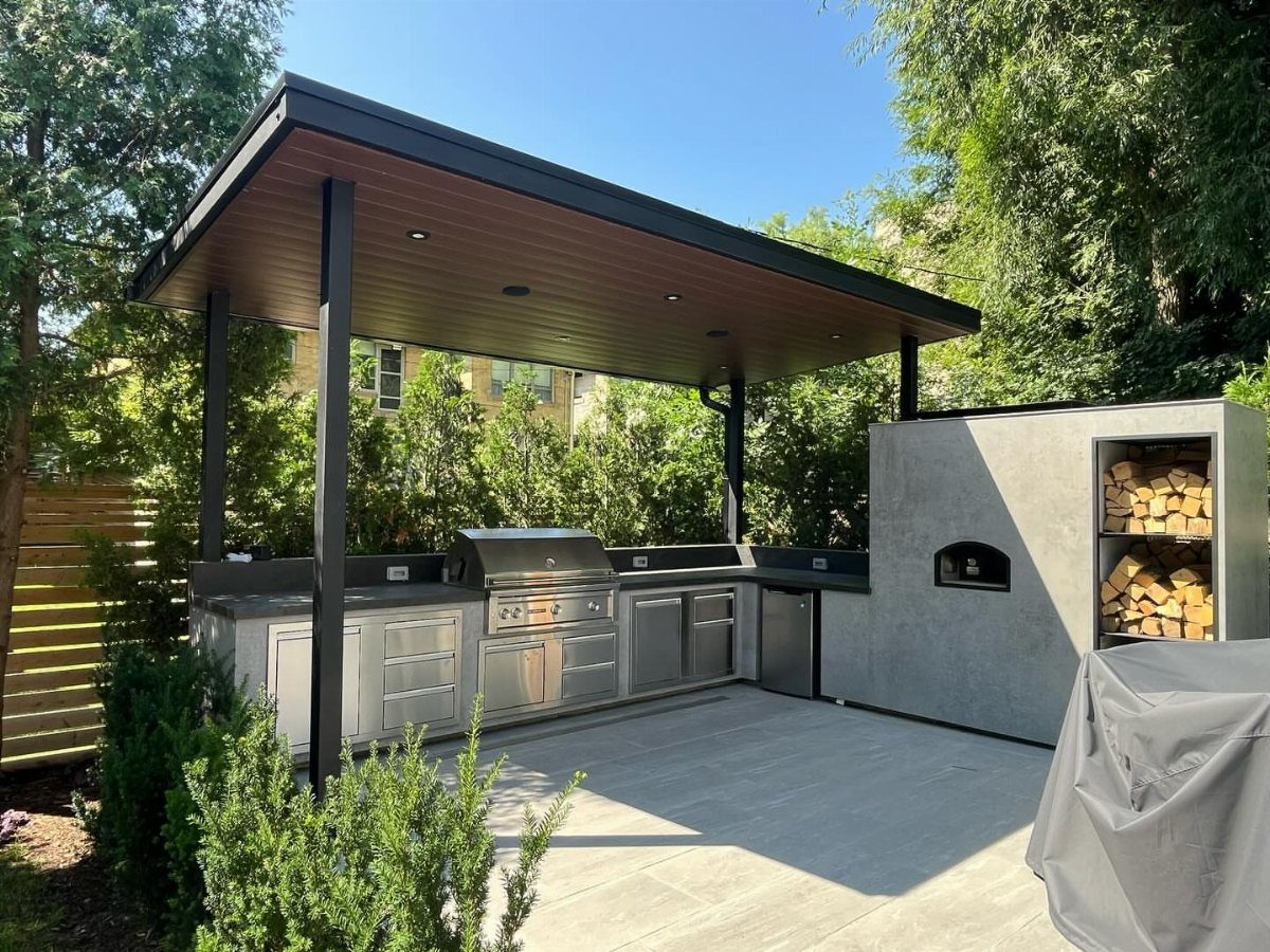 Modern outdoor kitchen with stainless steel appliances under a dark flat-roof canopy.