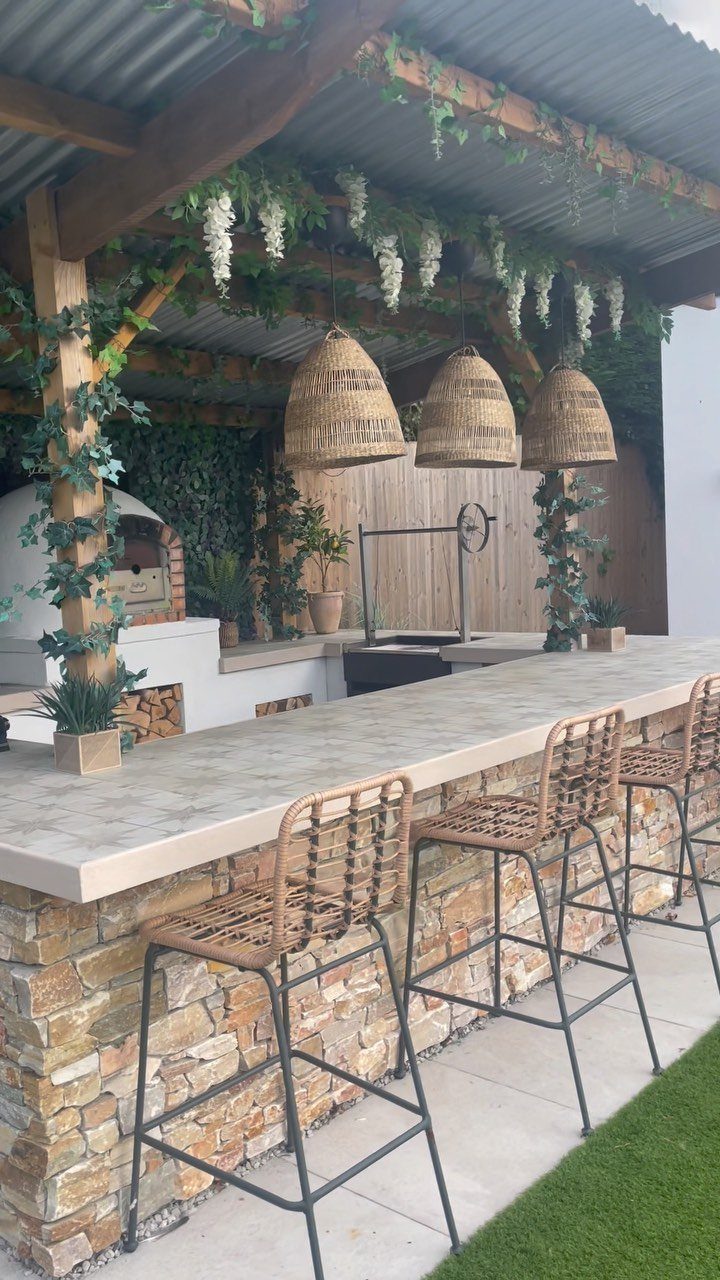 Outdoor kitchen bar with stone base, woven pendant lights, and a pizza oven.