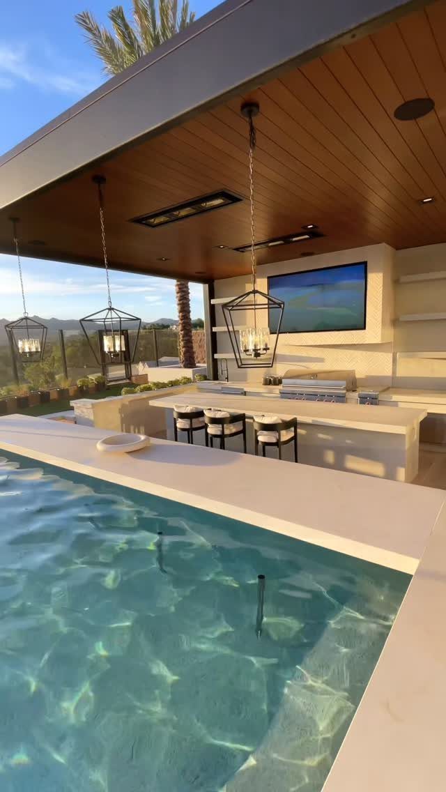 Modern outdoor kitchen with white bar, hanging lanterns, and adjacent swimming pool.