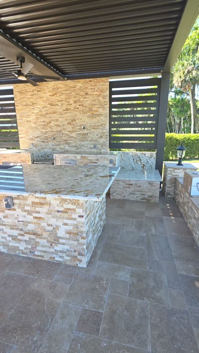 Modern outdoor kitchen with stacked stone counters, granite tops, and a dark pergola.