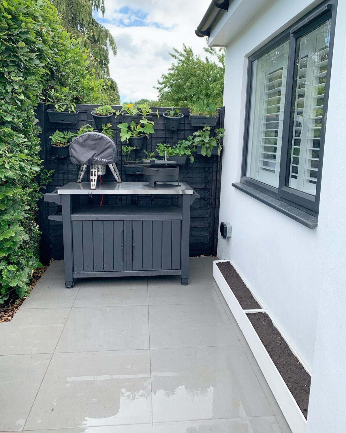 Grey outdoor kitchen station with wall-mounted planters creating a vertical garden on a fence