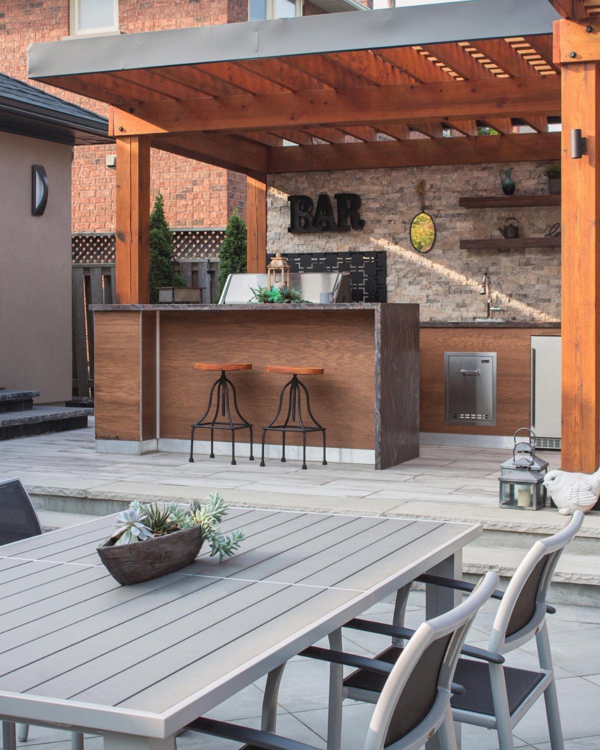 Outdoor kitchen bar with a dark waterfall countertop under a wooden pergola.