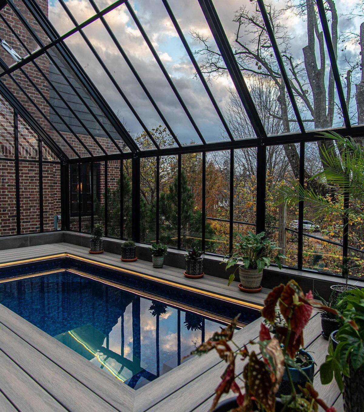 Indoor swimming pool enclosed in a black-framed glasshouse with a wooden deck.