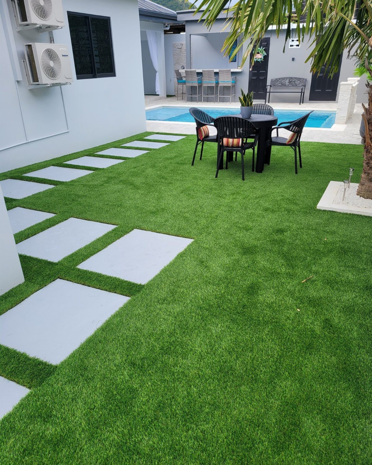 Artificial grass lawn with white stepping stones leading to a blue swimming pool.