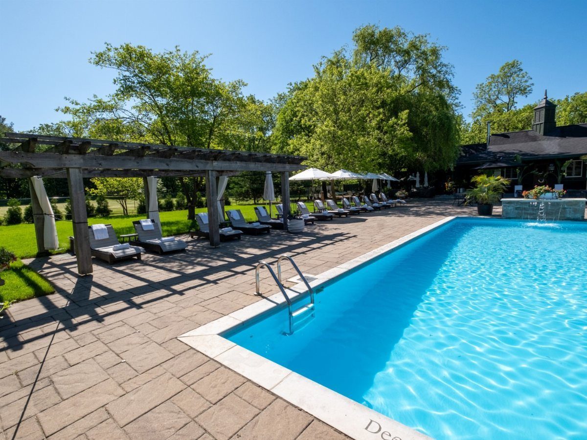 Rectangular blue swimming pool with stone patio, wooden pergola, and lounge chairs.