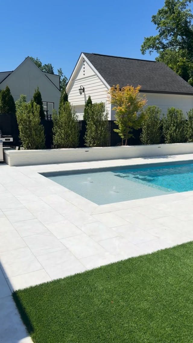 Modern swimming pool with white stone patio and a separate green grass lawn.