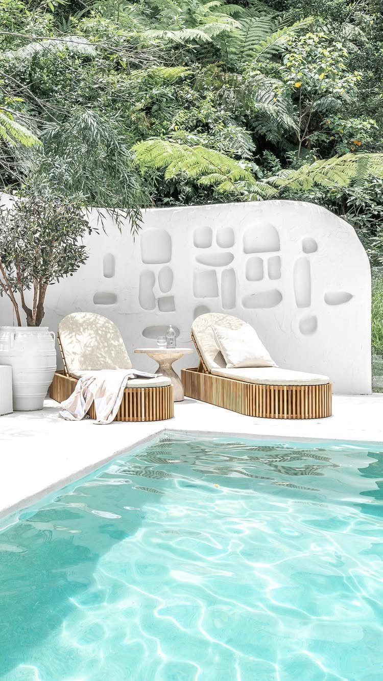 Turquoise swimming pool with wooden lounge chairs and a white textured accent wall.