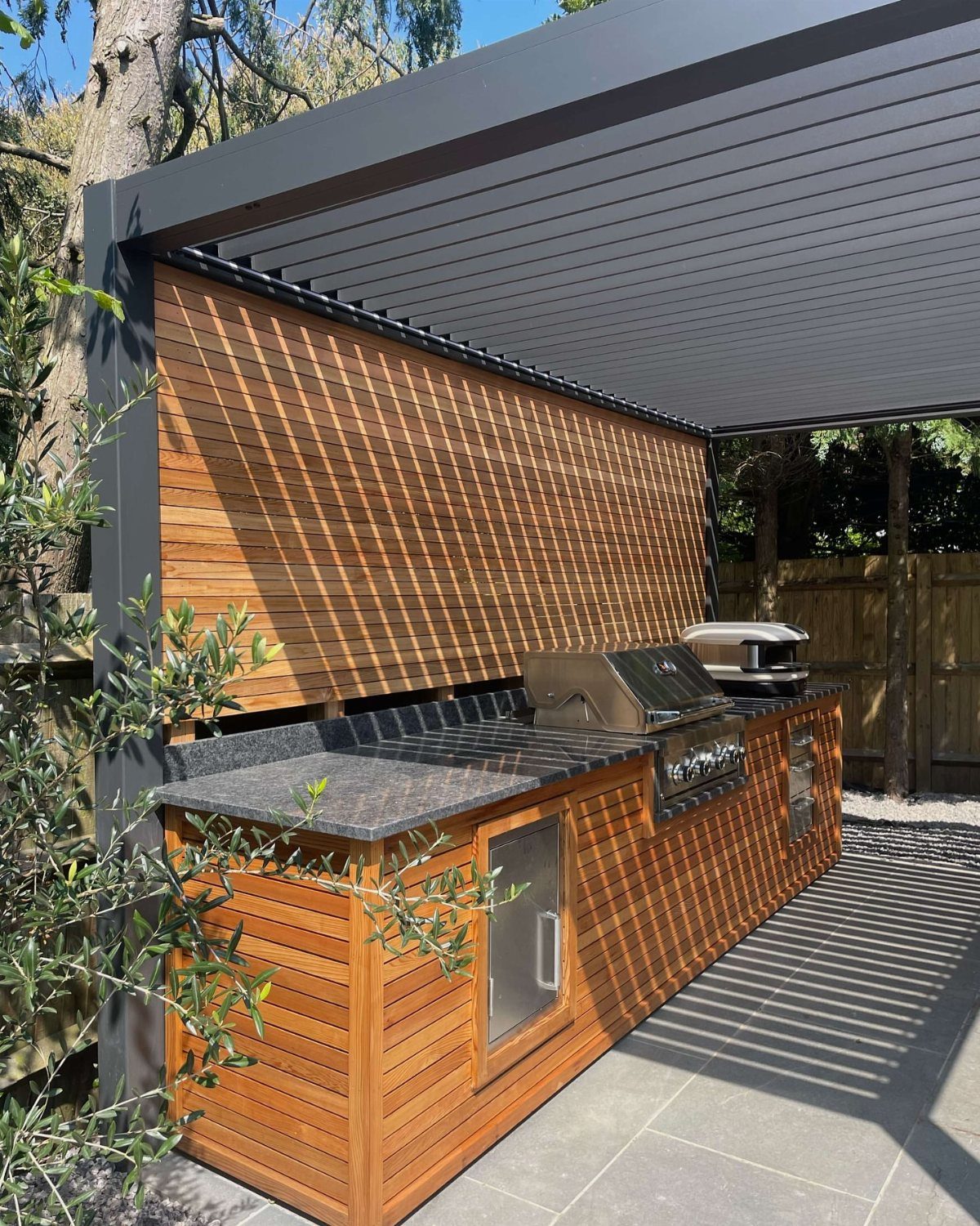 Outdoor kitchen with built-in grill and wood slat cabinetry under a modern pergola.