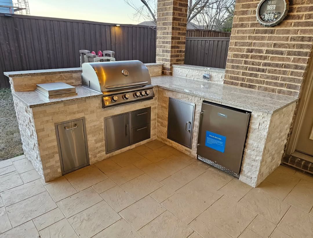L-shaped outdoor kitchen with stone cladding, built-in grill, and small refrigerator on patio.
