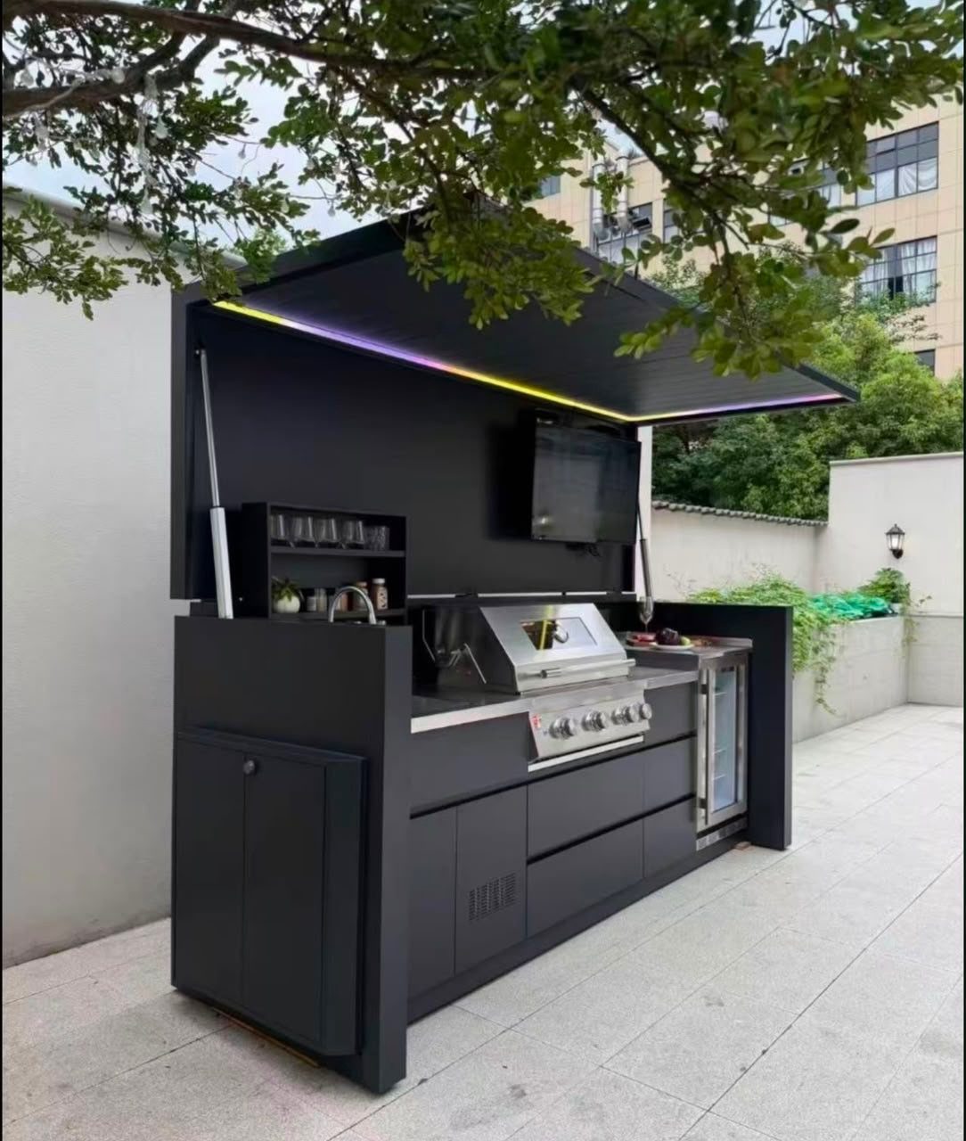 Modern black outdoor kitchen island with built-in grill, sink, and retractable canopy.