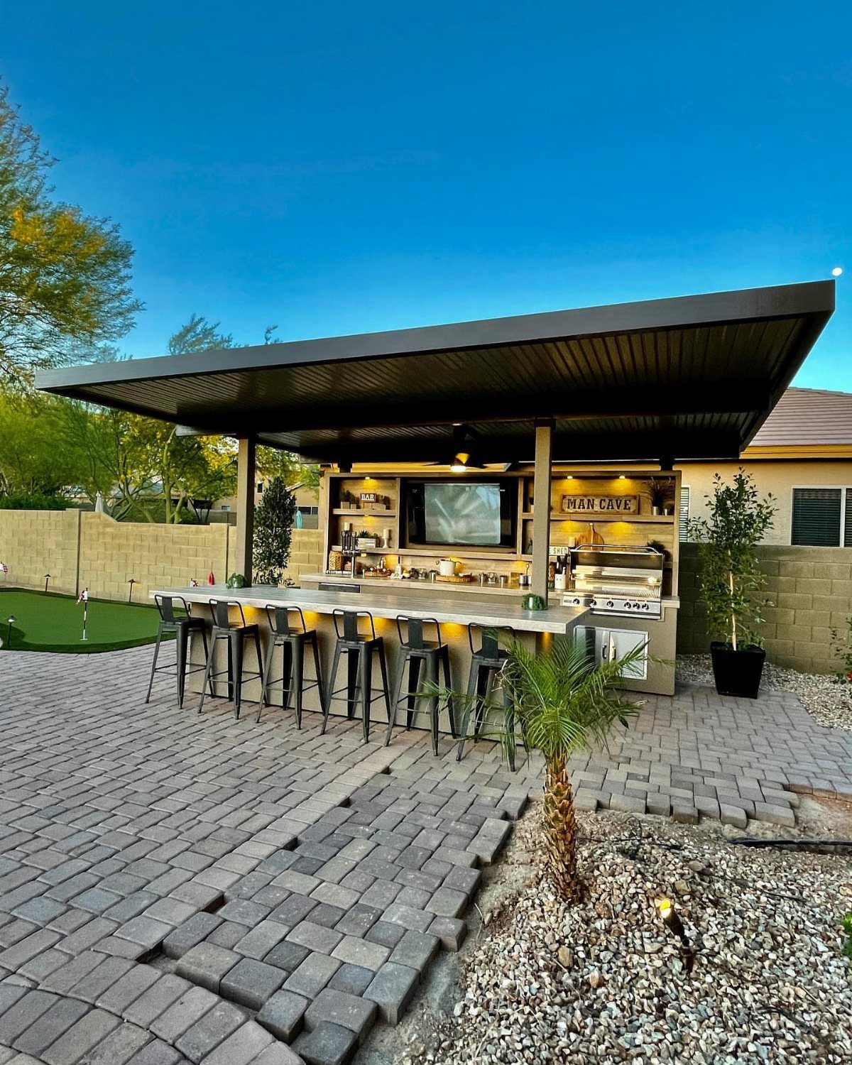 Modern outdoor bar with white countertop, black stools, and a beverage center.