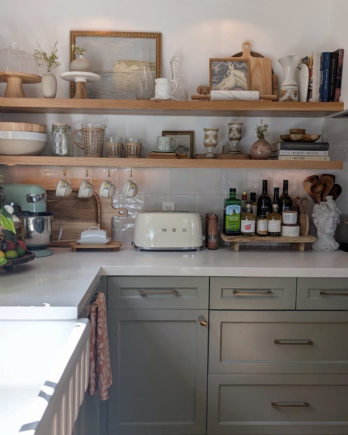 Wooden open shelves holding kitchenware above grey cabinets and a white countertop.