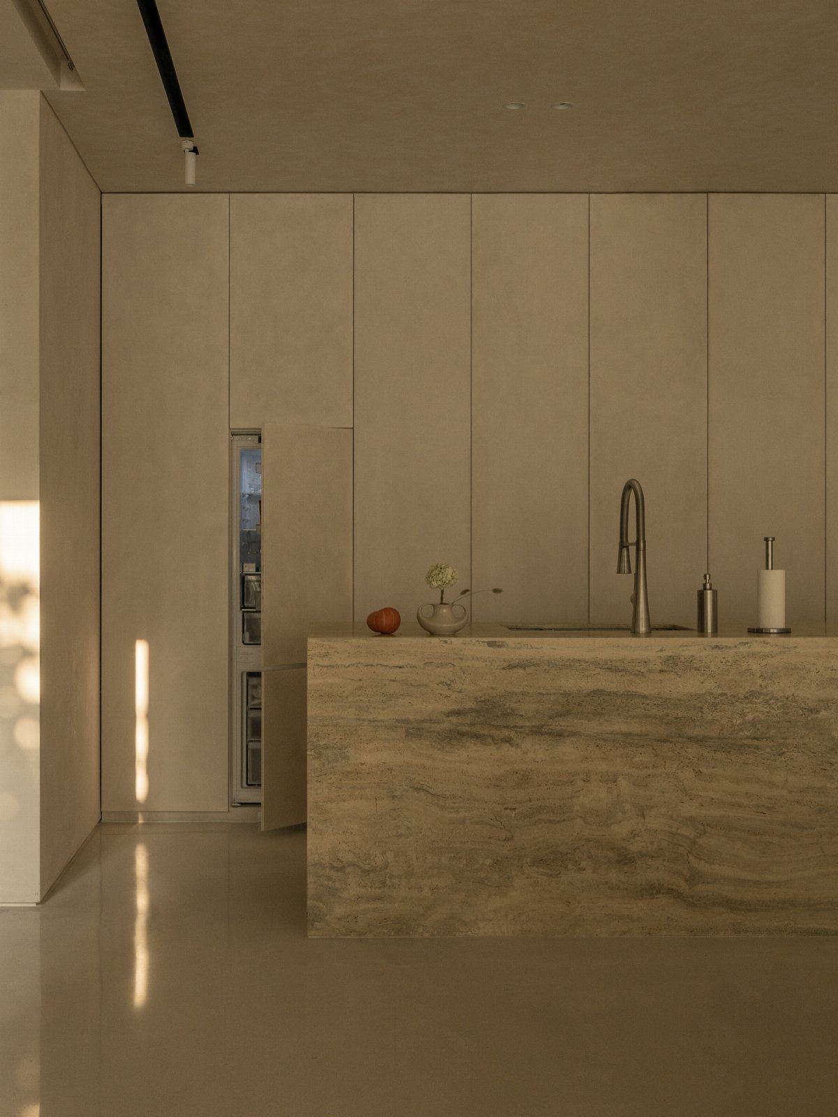 Minimalist kitchen with a beige marble island and seamless floor-to-ceiling cabinetry.