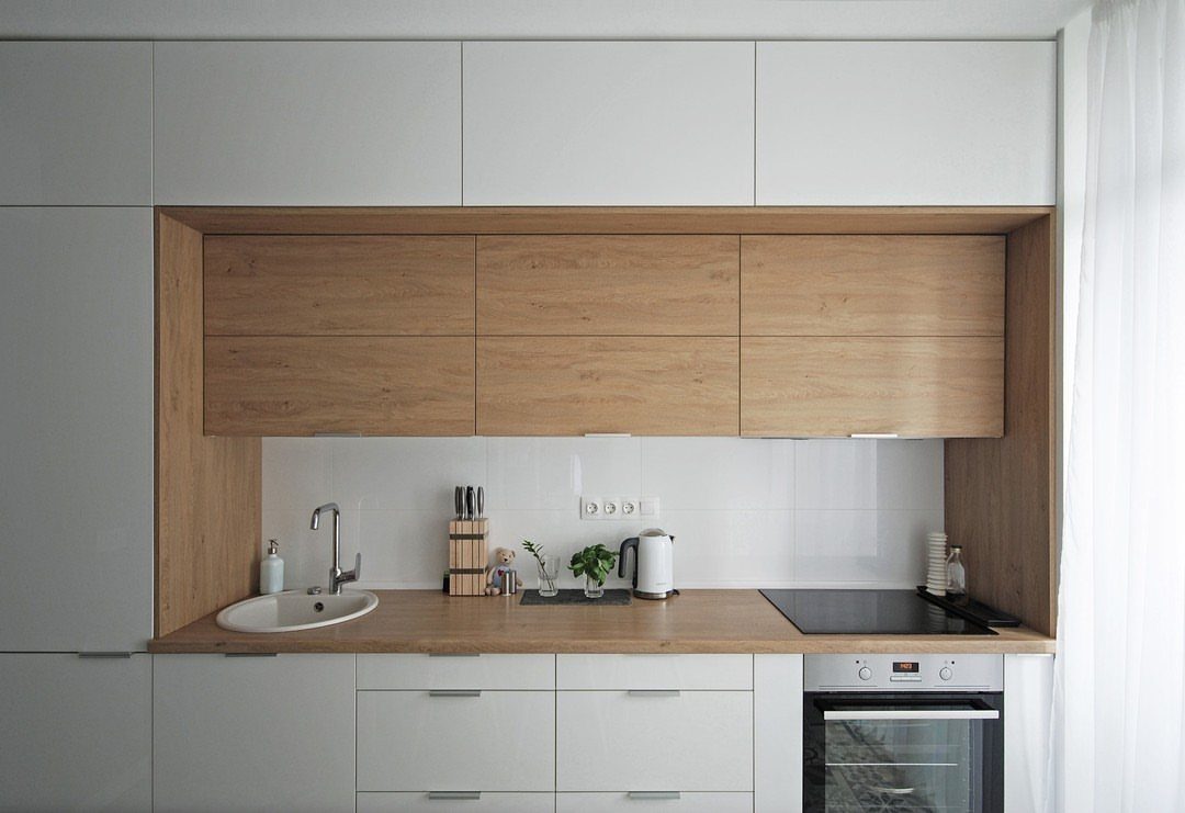 Single-wall kitchen with white and wood cabinets, integrated oven, and small sink.