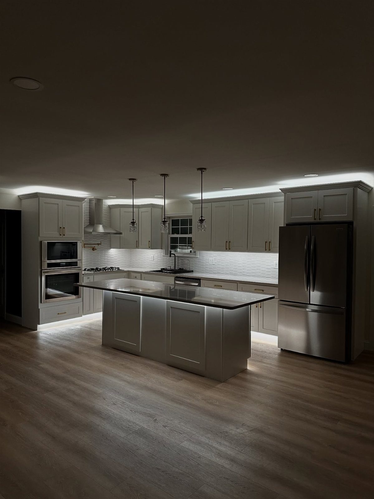 Modern grey kitchen featuring bright under-cabinet lighting and a central island with countertops.